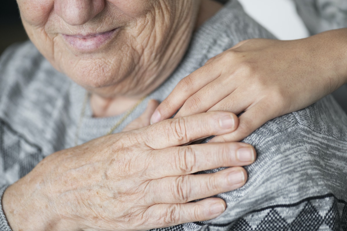 close up of a shoulder and face of an elderly person, their hand in holding someone else's hand which is over their shoulder