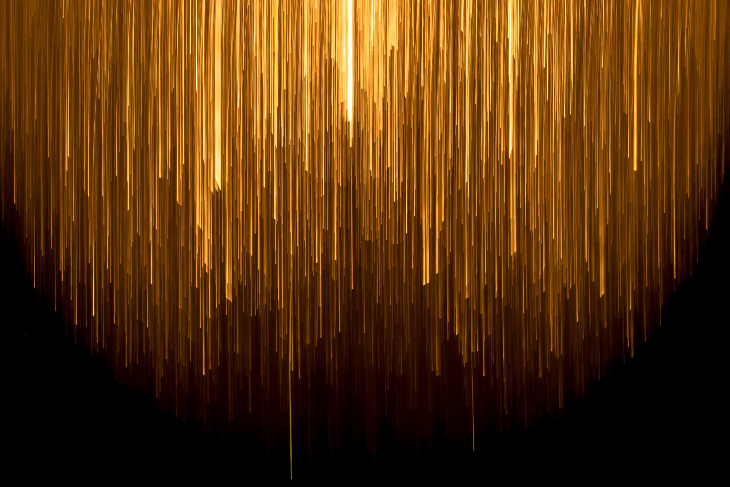 abstract image, looks like golden ribbons placed vertically in different lengths against a dark background