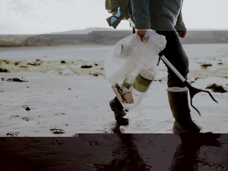 person walking on a beach carrying a device to pick litter and a plastic bag to put litter inside