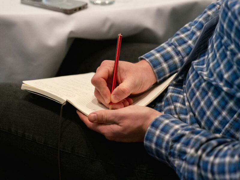 A photo of a man writing in a pad with a pencil