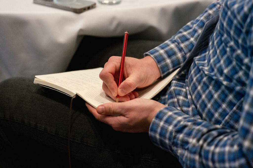 A photo of a man writing in a pad with a pencil