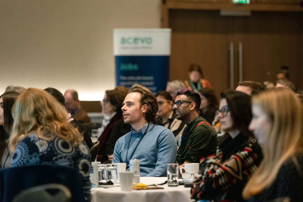 A photo of people sat at tables in a conference room